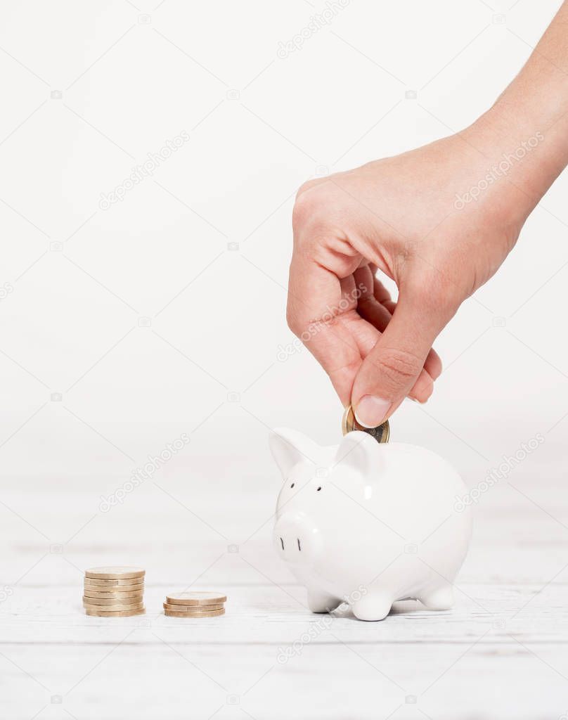 Piggy Bank and Coin in Female Hands over the white wooden background