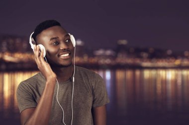 Kulaklık ile müzik dinleme sırasında sahilde yürüyen mutlu Afrika adam.