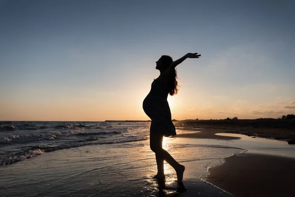 Silhueta de mulher grávida fazendo ioga e exercício na praia no pôr do sol do mar . — Fotografia de Stock