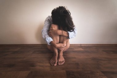 bir duvarının yakınında katta oturan ve bacaklarını onun elinde tutan bir üzgün kadın.