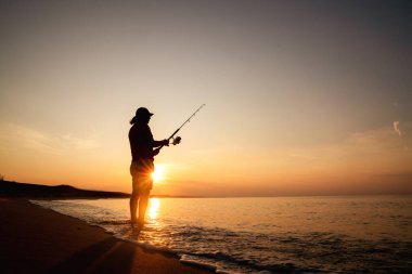 Sağlıklı bir yaşam için kumlu bir sahilde güneşin doğuşunda balık tutmak.