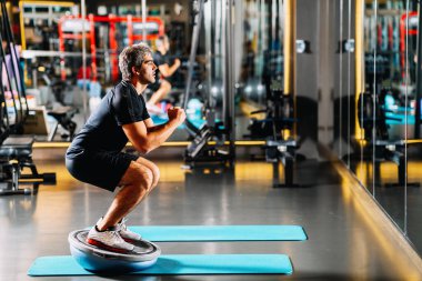 Genç ve atletik bir adam spor salonunda dengede duruyor.