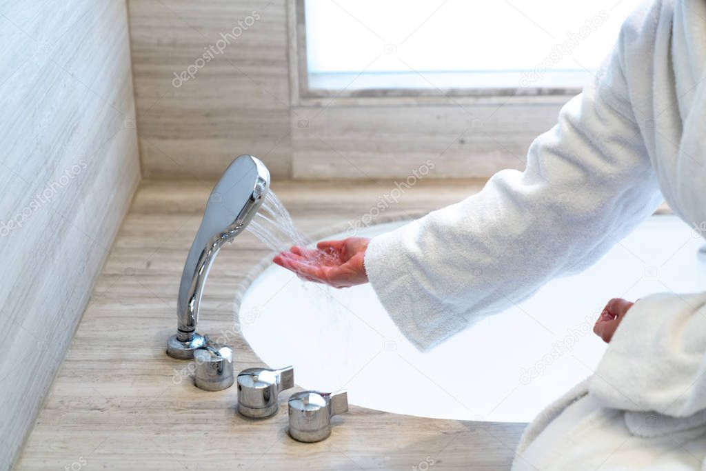 Woman is checking temperature touching running water with hand for having a bath