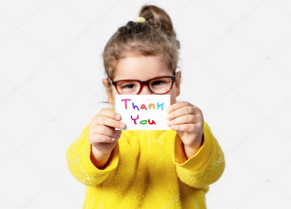 Adorable baby girl is holding a paper with a Thank you note. Silent communication concept.