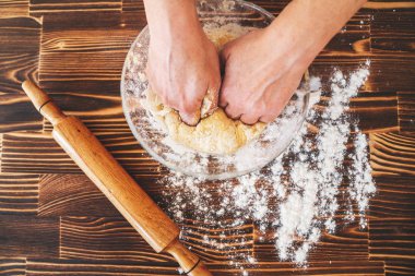 Kadın mutfakta hamur yoğuruyor, hamur tarifi malzemeleri ve yukarıdan eski ahşap bir masaya raptiye takıyor..