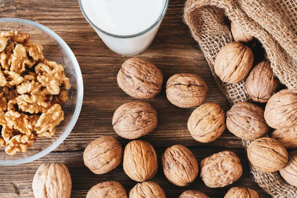 Close up top view of cracked walnuts and a glass of milk on a wooden table. Healthy life concept. — Stock Photo, Image