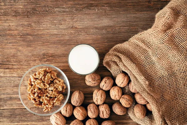 Close up top view of cracked walnuts and a glass of milk on a wooden table. Healthy life concept. — Stock Photo, Image