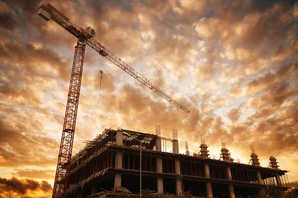 Silueta de un edificio con una grúa de construcción contra la puesta del sol y las nubes. Edificios y concepto de construcción . — Foto de Stock