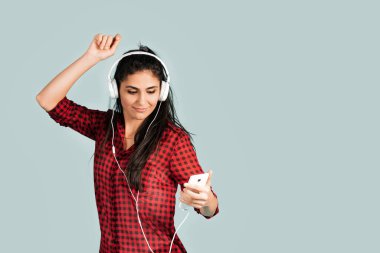 Beyaz kulaklıklı enerji kızı müzik dinliyor ve stüdyoda mavi arka planda dans ediyor..