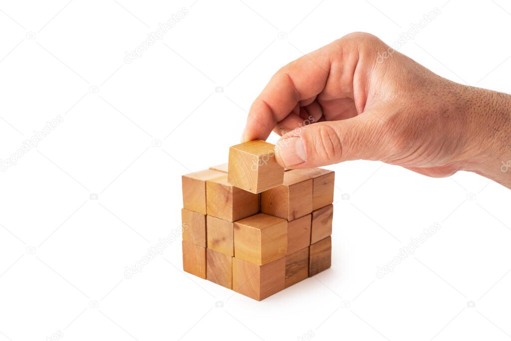 A hand is putting the last cube for building a cube with wooden cubes on white background. Success, strategy, teamwork and victory concept.