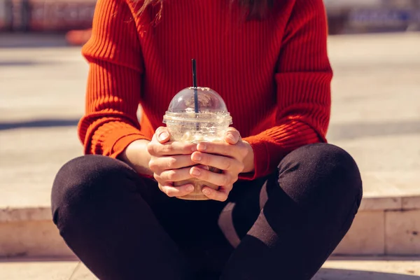 Mujer está sentada y sosteniendo una taza de eliminación de un delicioso frappe . — Foto de Stock