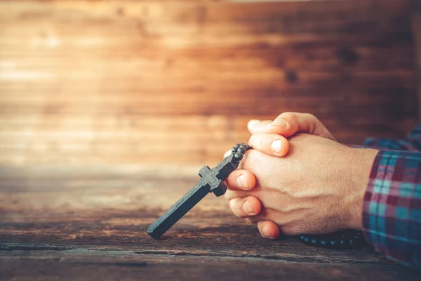 Les mains tiennent un crucifix et une vieille Bible de houx couverte et prient sur un fond de bois rustique . — Photo