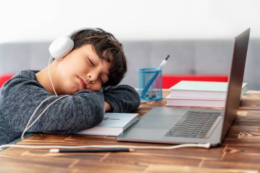 Yorgun küçük çocuk internette çalışırken dizüstü bilgisayarın başında uyukluyor..