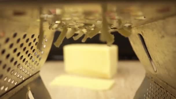 La mano sfrega il formaggio su una grattugia, e in lontananza è un pezzo di formaggio — Video Stock