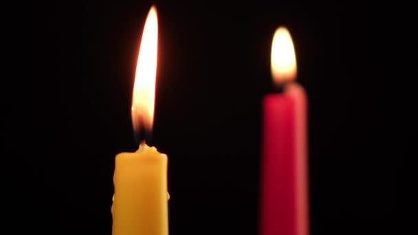 Dos velas rojas y amarillas se apagan sobre un fondo negro — Vídeos de Stock