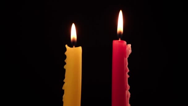 Dvě hořící svíčky červené a žluté na černém pozadí — Stock video