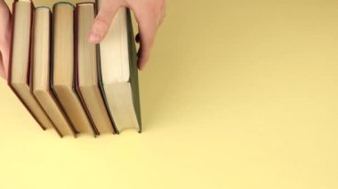 Bir erkeğin eli arka plana bir yığın kitap koyar.