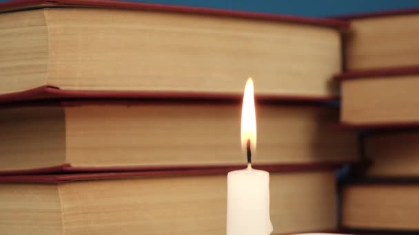 Uma única vela branca queima contra uma pilha de livros — Vídeo de Stock