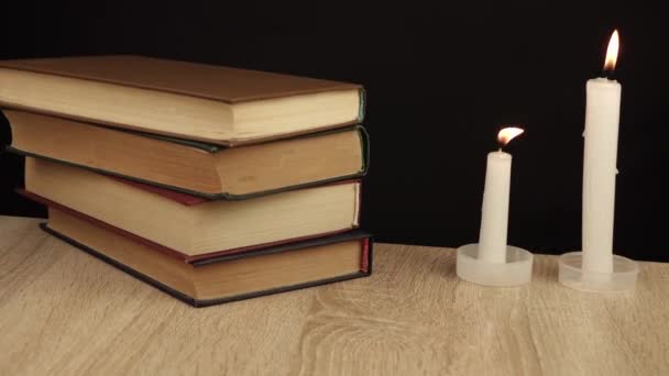 2 kaarsen op een zwarte achtergrond en een stel boeken op elkaar liggend — Stockvideo