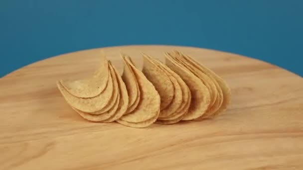 Hrst bramborových lupínků se otáčí o 360 stupňů na dřevěné plošině na modrém pozadí — Stock video