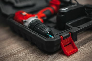 Kırmızı elektrikli matkap, siyah bir bavulun içinde, tahta bir masanın üzerinde..