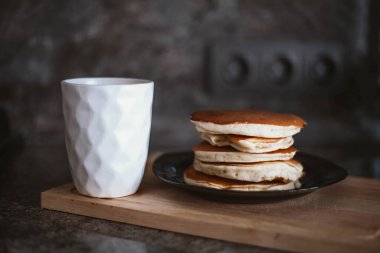 Beyaz bir kupa ve tabakta bir yığın krep.