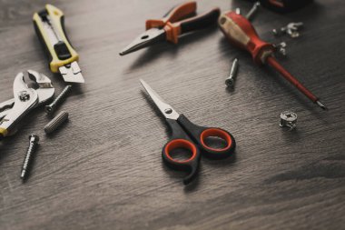 Ahşap bir masanın üzerinde bir yığın aletin arasında duran makas.