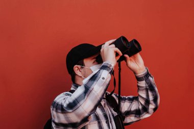 Bir adam kırmızı arka plandaki dürbünden yukarı bakar.