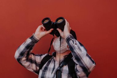 Bir adam kırmızı arka plandaki dürbünden yukarı bakar.