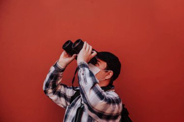 Bir adam kırmızı arka plandaki dürbünden yukarı bakar.