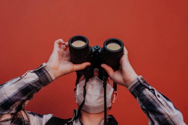 Bir adam kırmızı arka plandaki dürbünden yukarı bakar.