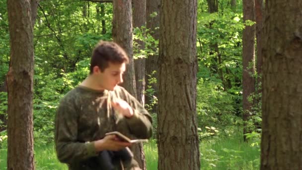 En man går genom skogen och skriver i sin dagbok — Stockvideo