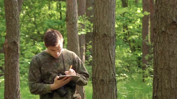 En man går genom skogen och skriver i sin dagbok — Stockvideo