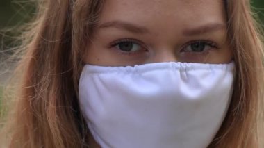 Beyaz maskeli bir kız sokakta duruyor. Kapat.