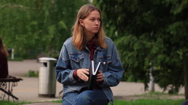 Ein Mädchen liest auf der Straße ein Buch, während es auf einer Bank sitzt — Stockvideo