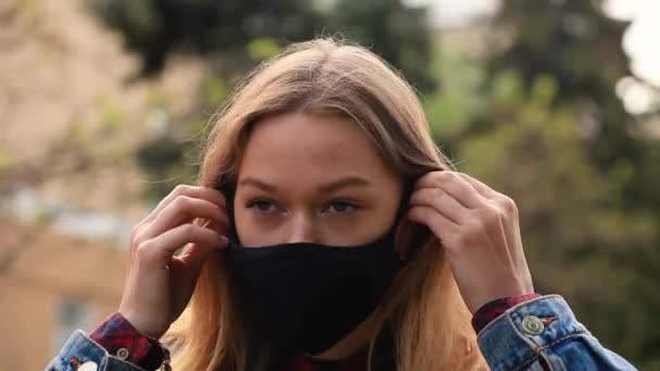 A girl puts a black mask on her face while standing on the street — Stock Video