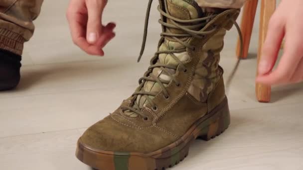 Een man die zijn camouflage laarzen optrekt voordat hij het gebouw verlaat. — Stockvideo