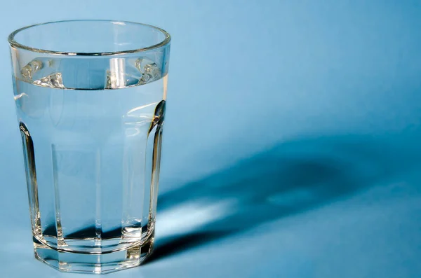 Wasserglas mit starken Schatten auf weißem Hintergrund — Stockfoto