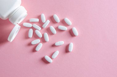 Beyaz tabletli beyaz plastik bir kap beyaz tabletlerin yanında çok renkli bir arkaplanda yatıyor.