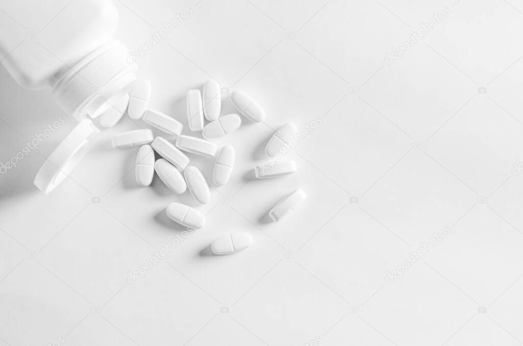 A white plastic container with white tablets lies on a white background next to white tablets