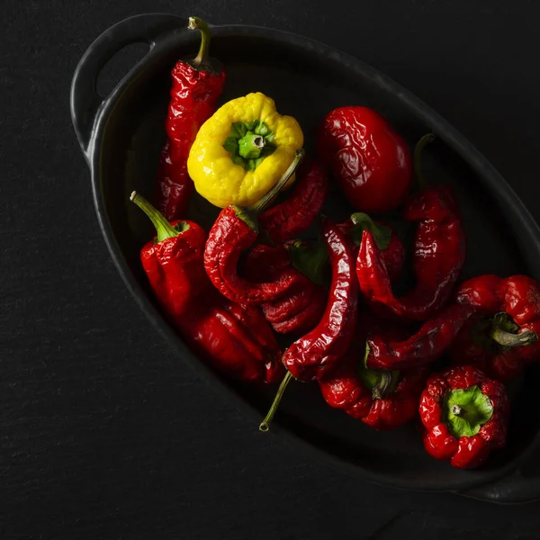 Dried multi-colored, textured chili peppers lie in black form for baking on a black stone background — Stock Photo, Image