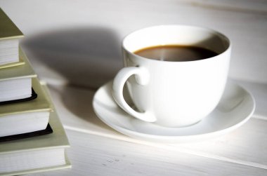 Yuvarlak, beyaz bir fincan kahve fincanın gölgesinin yanındaki beyaz bir tabağın üzerinde duruyor.