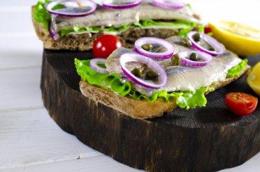 Tuzlanmış ringa balığı, tereyağı ve eski rustik kesme tahtası üzerinde kırmızı soğan ile sandviç. Seçici odak