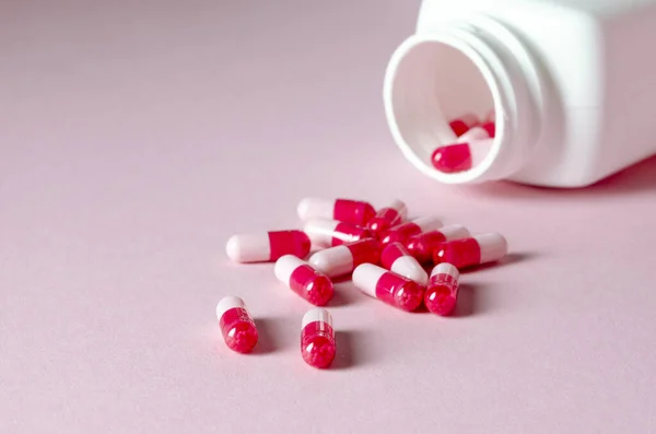 Red and white tablets lie on a pink background next to a white plastic container
