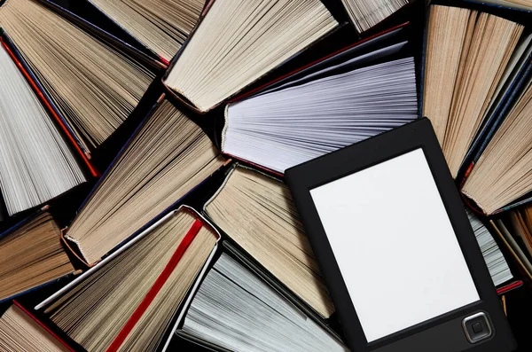 The e-book with a white screen lies on the open multi-colored books that lie on a dark background, close-up Royalty Free Stock Photos