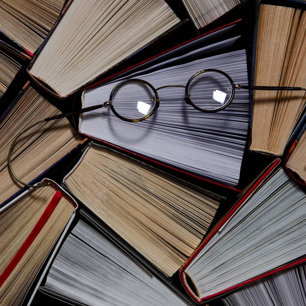 Mnoho pestrobarevné tlusté otevřené knihy stojí na tmavém pozadí. Na knihách jsou staré kulaté sklenice — Stock fotografie