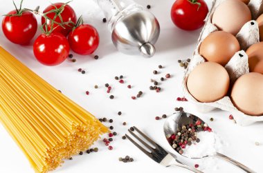 Spagetti, kiraz domates, kaşık ve çatal ile birlikte, beyaz bir arka plan üzerinde yalan