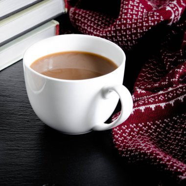 Yuvarlak beyaz bir fincan ve çay tabağı kitapların ve sarı sonbahar yapraklarının yanında beyaz bir ahşap masanın üzerinde duruyor.