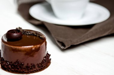 Bir ahşap stand yanında beyaz bir masada duran beyaz bir fincan lezzetli çikolatalı pasta çikolata parçaları ile yatıyor