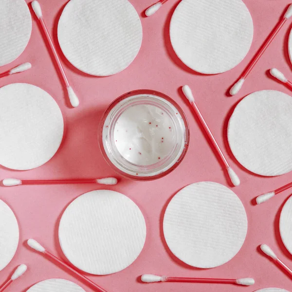 Higiéniai termékek: fehér kerek pamut párnák és műanyag rudak tisztítására a fül fekszik egy rózsaszín háttér mellett arckrém — Stock Fotó